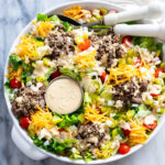 A white bowl with Big Mac Salad with big mac salad dressing, lettuce, ground beef, cheese, pickles, onions, and tomatoes.