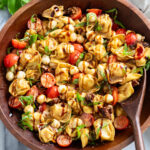 Caprese Pasta Salad in a wooden bowl with balsamic glaze drizzled on top with fresh basil.