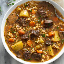 Hearty Beef Barley Soup in a white bowl with fresh parsley on top and a spoon on the side.